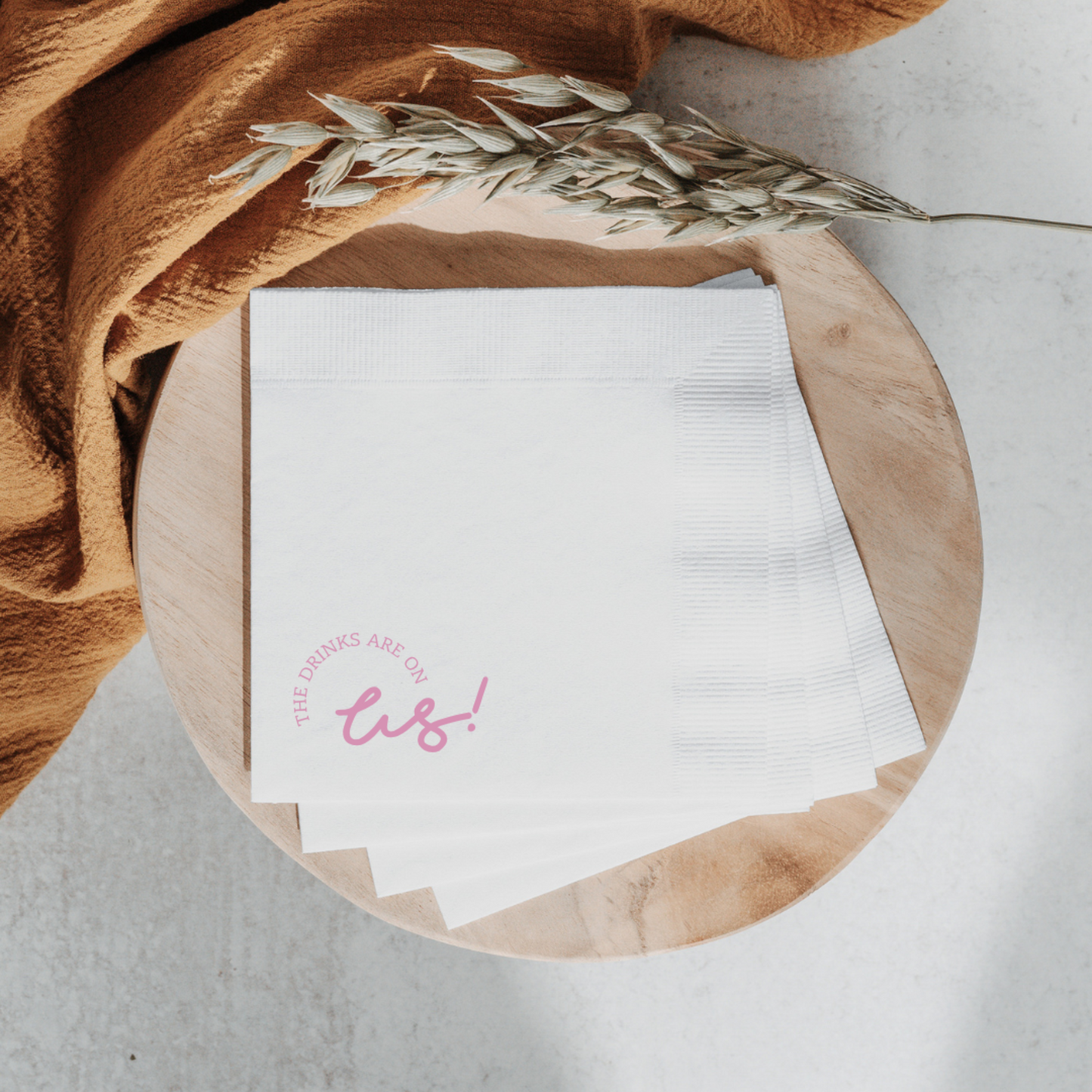 Custom cocktail napkin with pink 'The drinks are on us!' text, perfect for wedding bar signage or party stationery