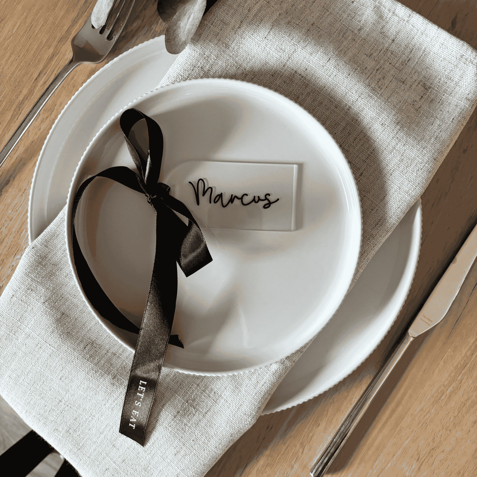 Acrylic wedding place setting with black ribbon on linen napkin, styled table setting with custom wedding stationery