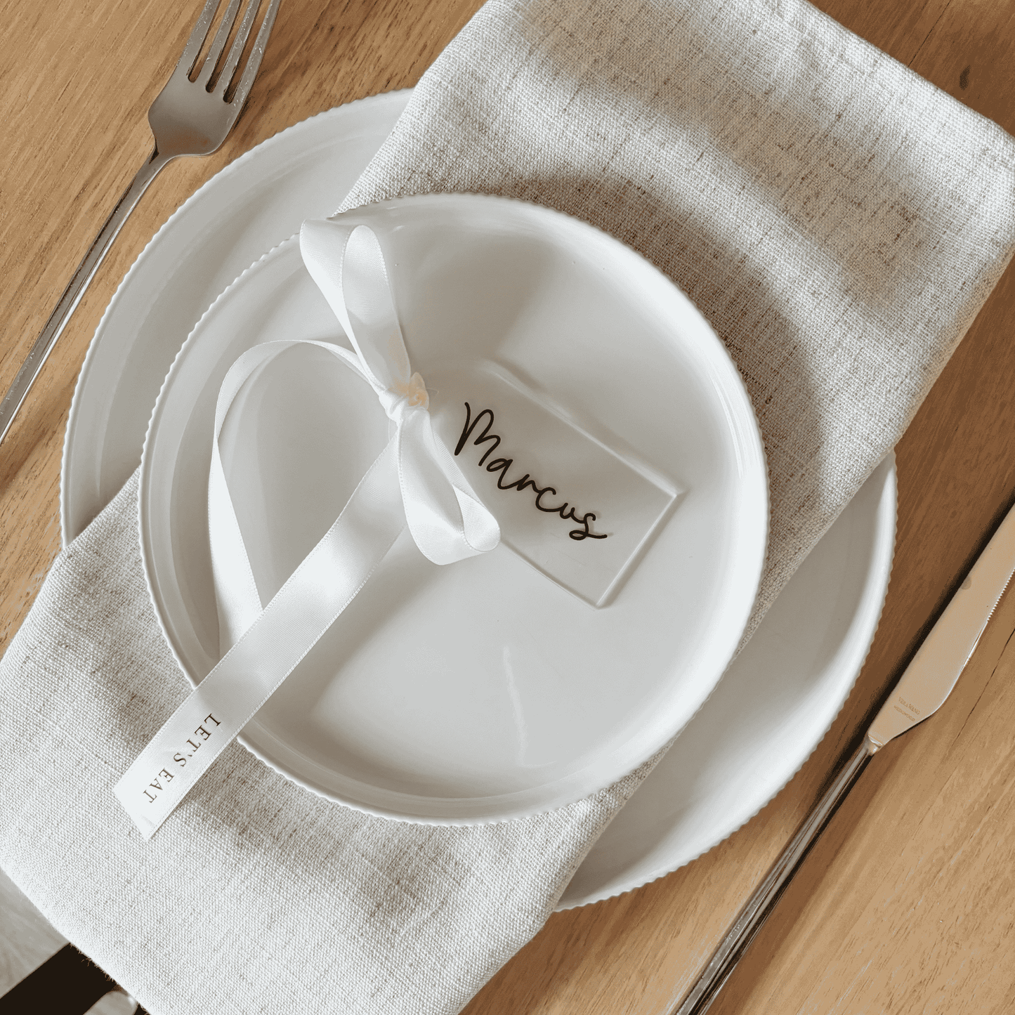 Clear arch acrylic place card with black lettering and white ribbon, part of custom wedding invitations and table settings