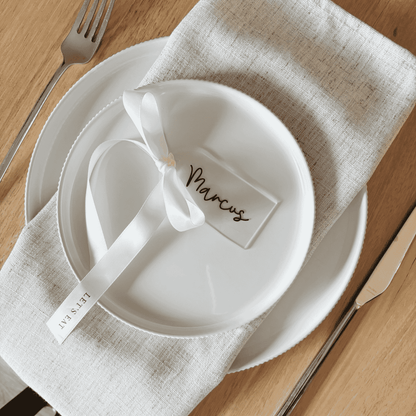 Clear arch acrylic place card with black lettering and white ribbon, part of custom wedding invitations and table settings