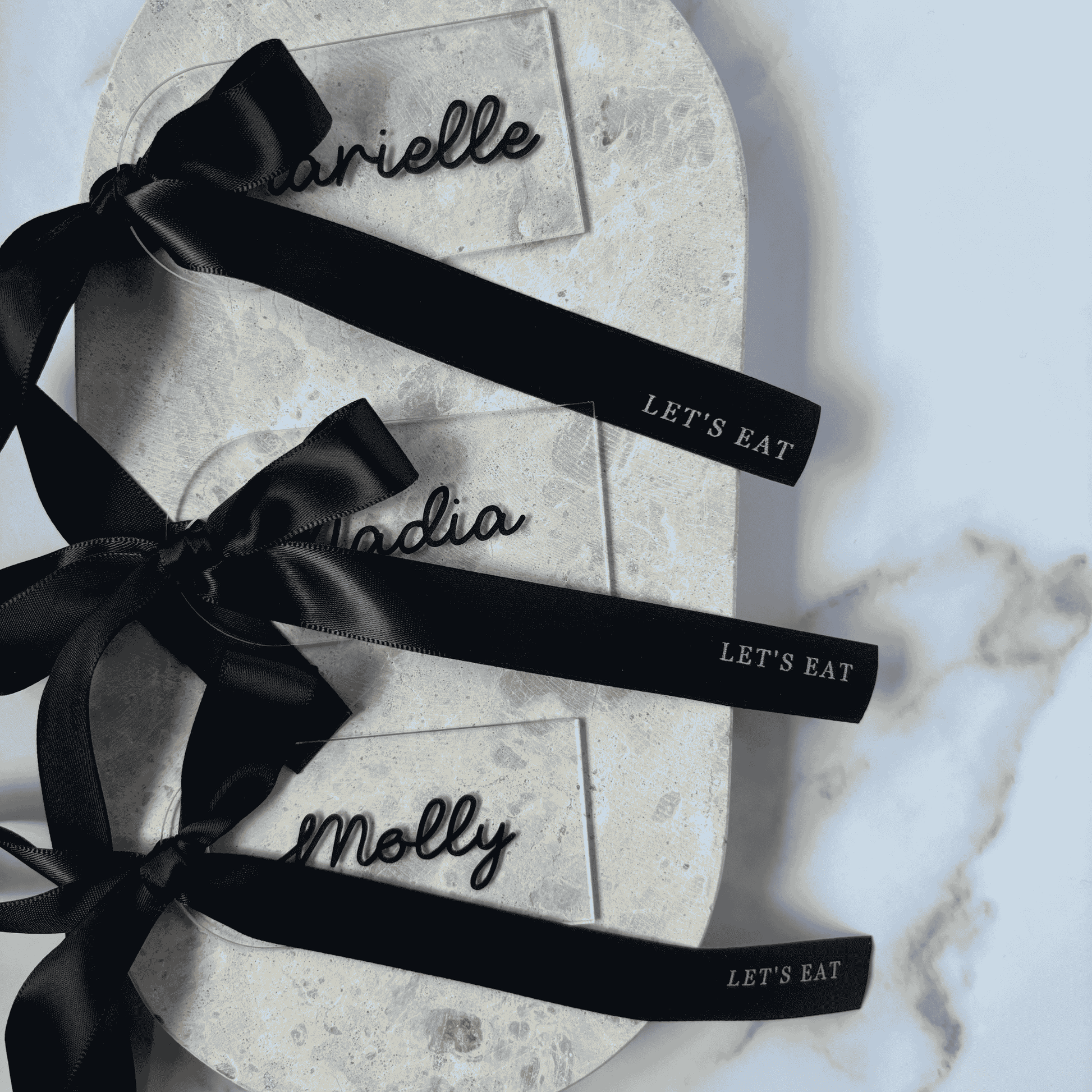 Set of clear acrylic wedding place cards with black names and black ribbons, styled for wedding table settings