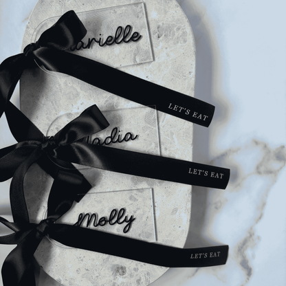 Set of clear acrylic wedding place cards with black names and black ribbons, styled for wedding table settings