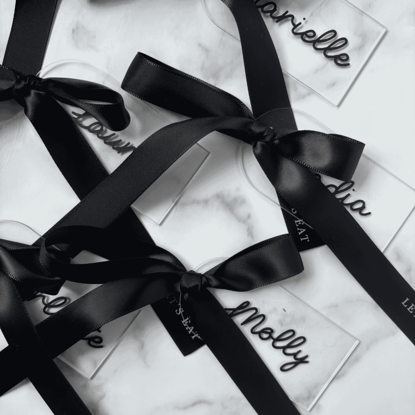 Set of clear acrylic wedding place settings with black names and satin ribbons, styled for modern wedding table settings