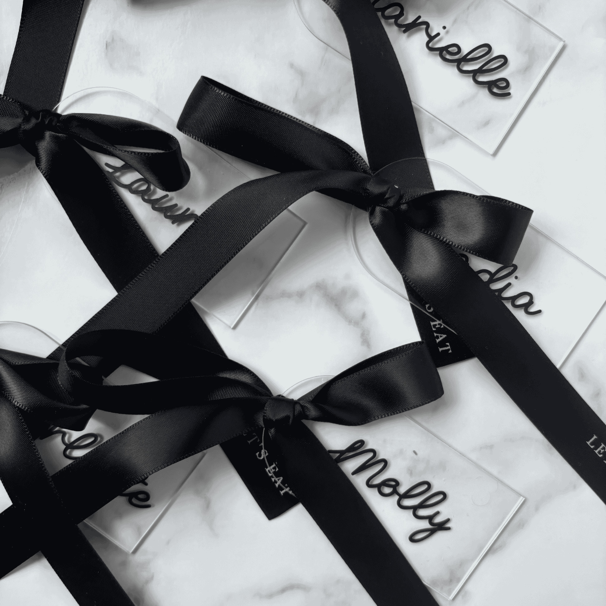 Set of clear acrylic wedding place settings with black names and satin ribbons, styled for modern wedding table settings
