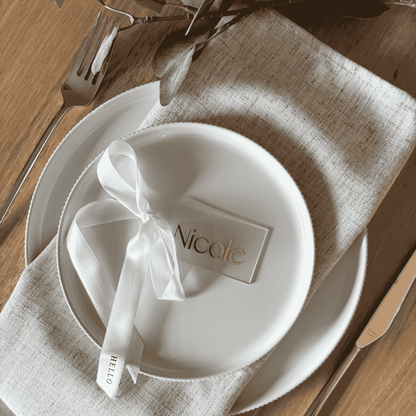 Personalised acrylic wedding place setting with gold name and white ribbon, styled for refined wedding table settings