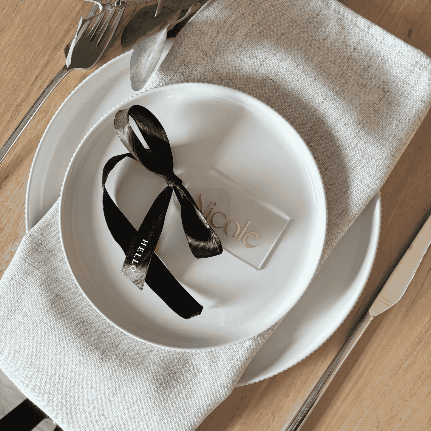 Clear acrylic wedding place setting with gold lettering and black ribbon, styled on a linen napkin for wedding table settings