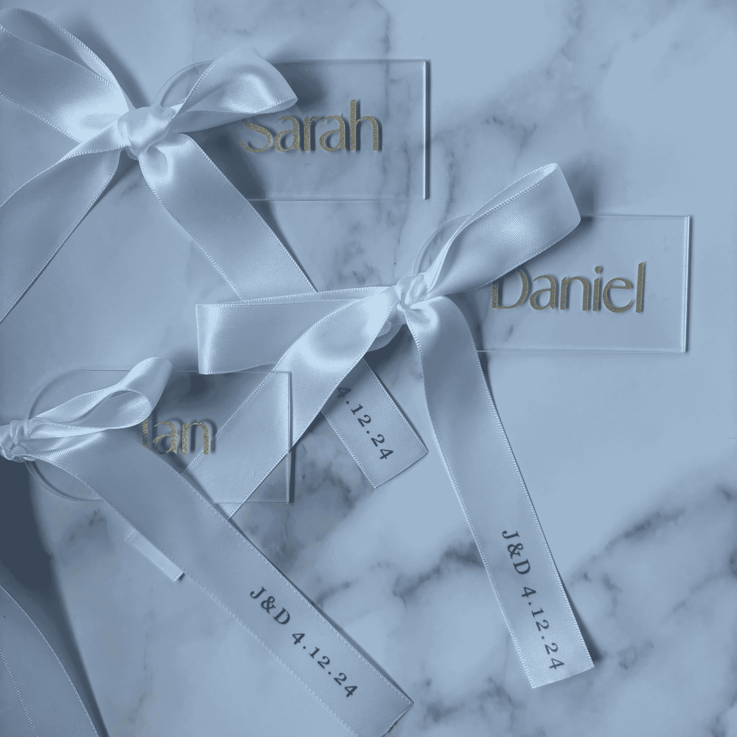 Set of white and gold acrylic wedding place settings with ribbon, styled alongside coordinated wedding stationery