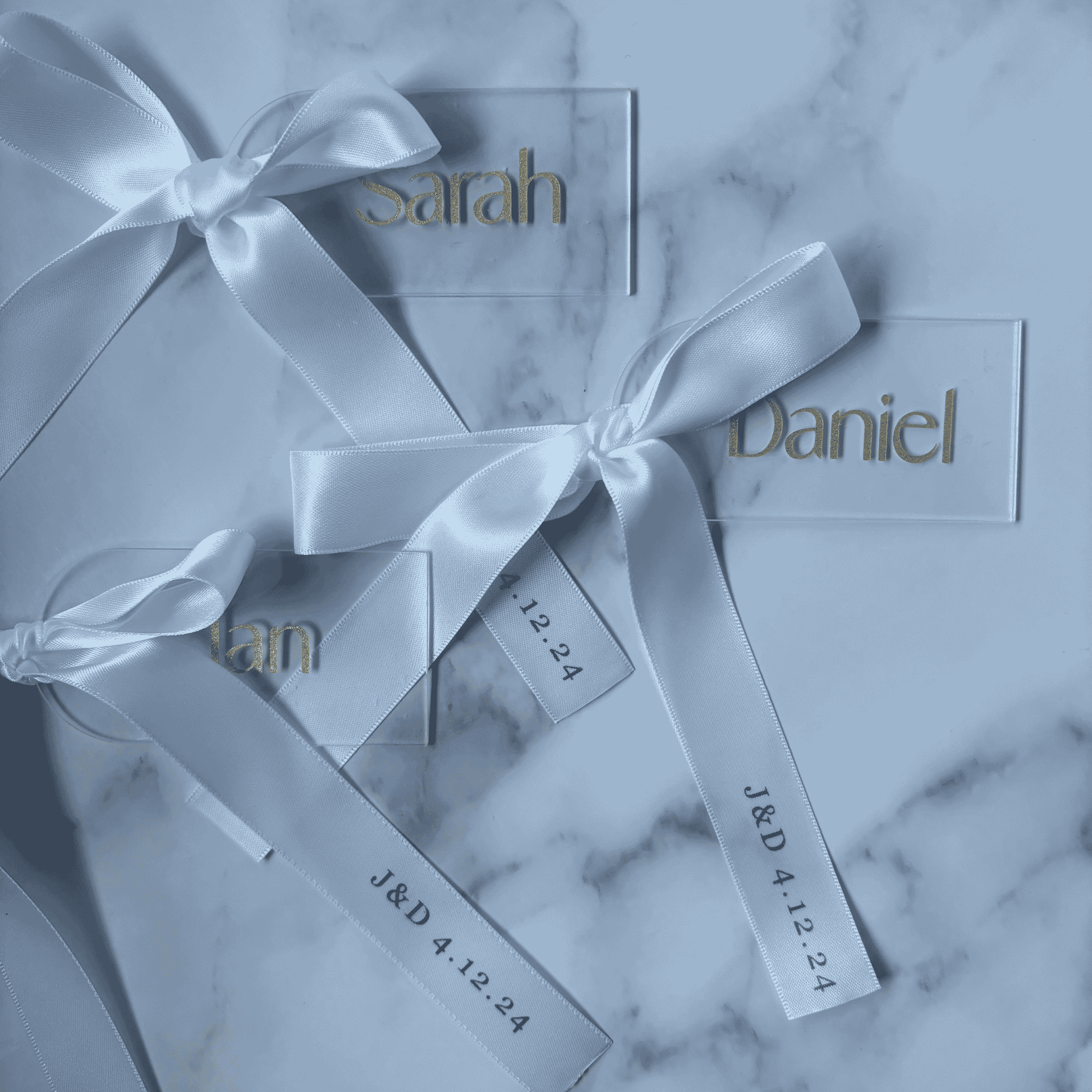 Set of white and gold acrylic wedding place settings with ribbon, styled alongside coordinated wedding stationery