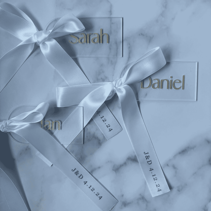 Set of white and gold acrylic wedding place settings with ribbon, styled alongside coordinated wedding stationery