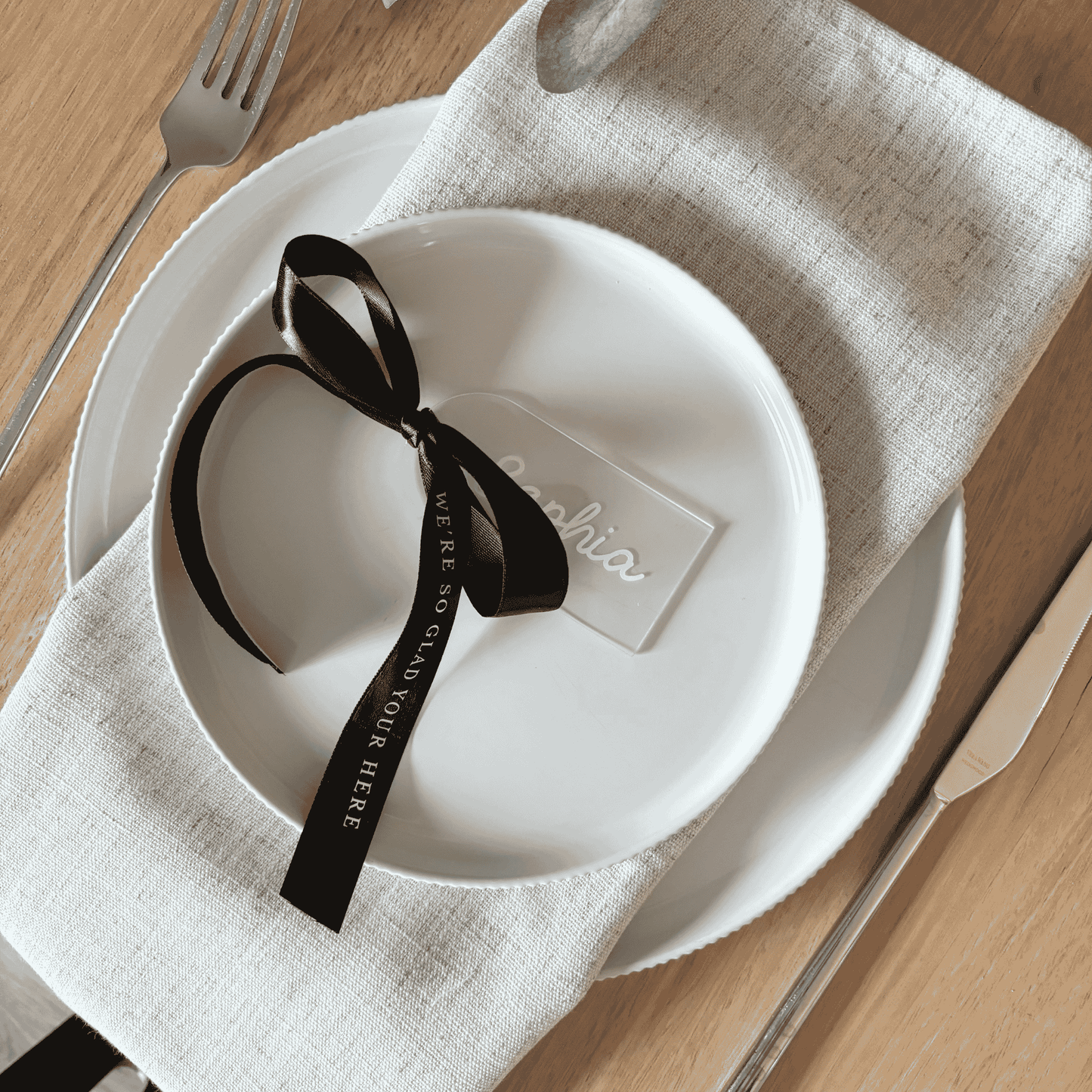 Clear acrylic wedding place setting with white name and black ribbon, styled for modern wedding table settings