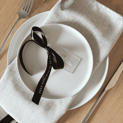 Clear acrylic wedding place setting with white name and black ribbon, styled for modern wedding table settings