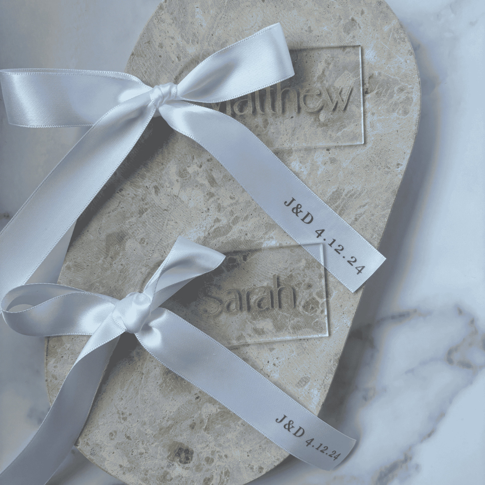 Clear acrylic wedding place setting tied with white ribbon, styled on stone for coordinated wedding stationery