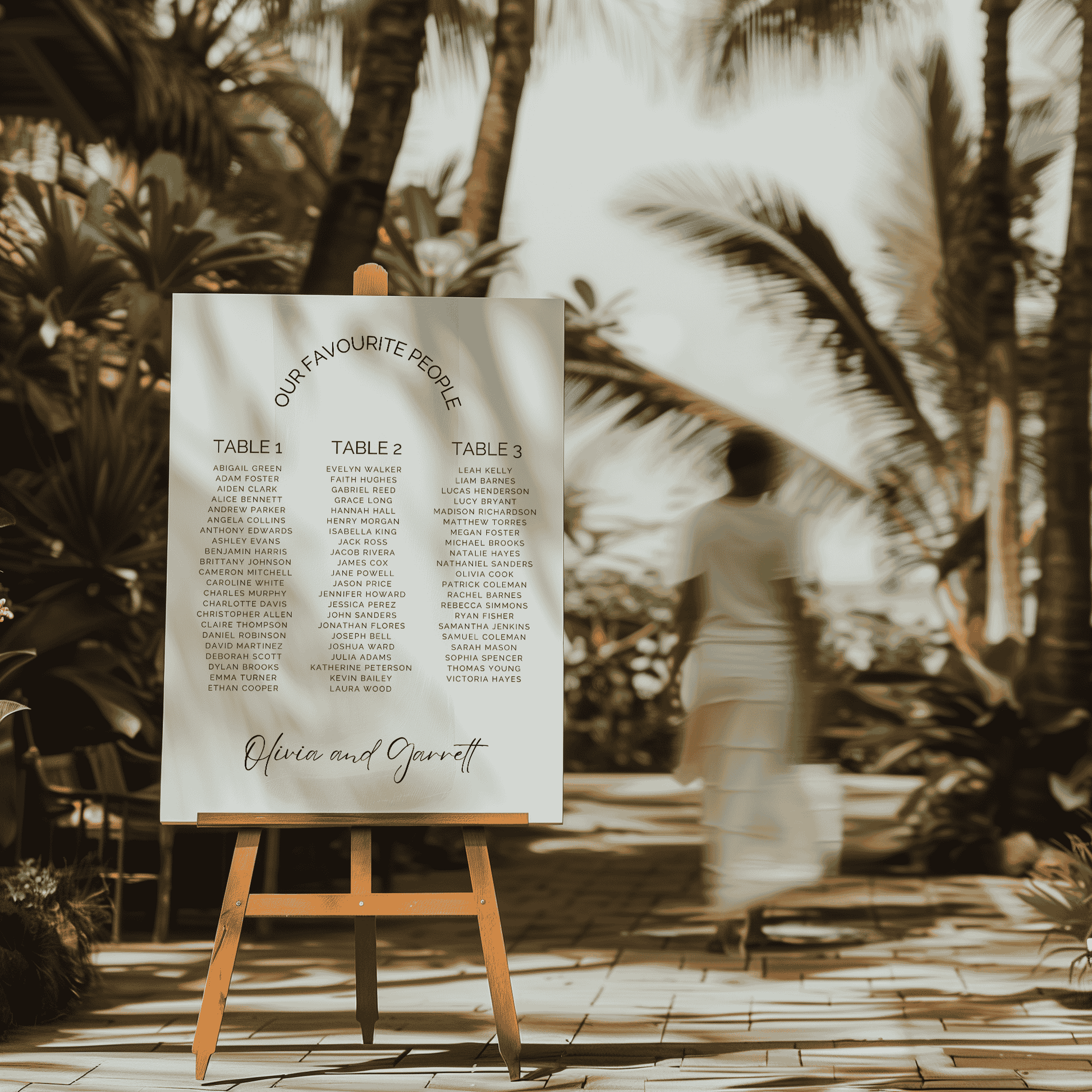 Classic wedding seating chart displayed on easel at tropical beach venue with soft sunset light and palm surrounds
