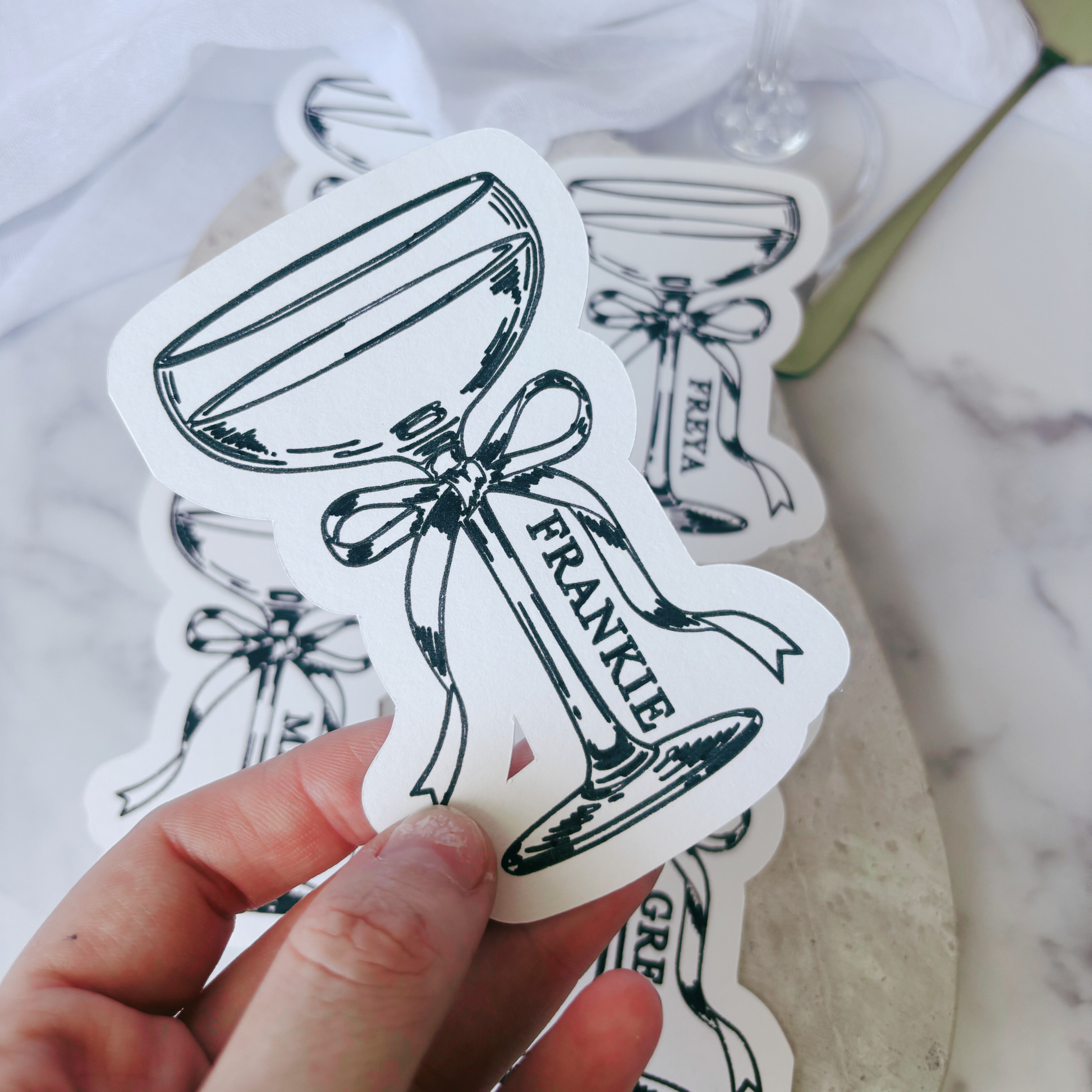 Close-up of white cocktail-themed place cards with illustrated coupe glass, personalised for wedding table settings