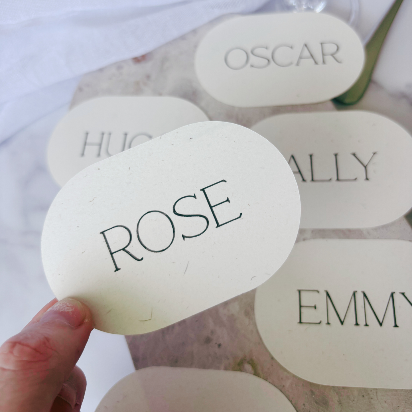 Close-up of ivory oval wedding place card with guest name, featuring soft textured cardstock