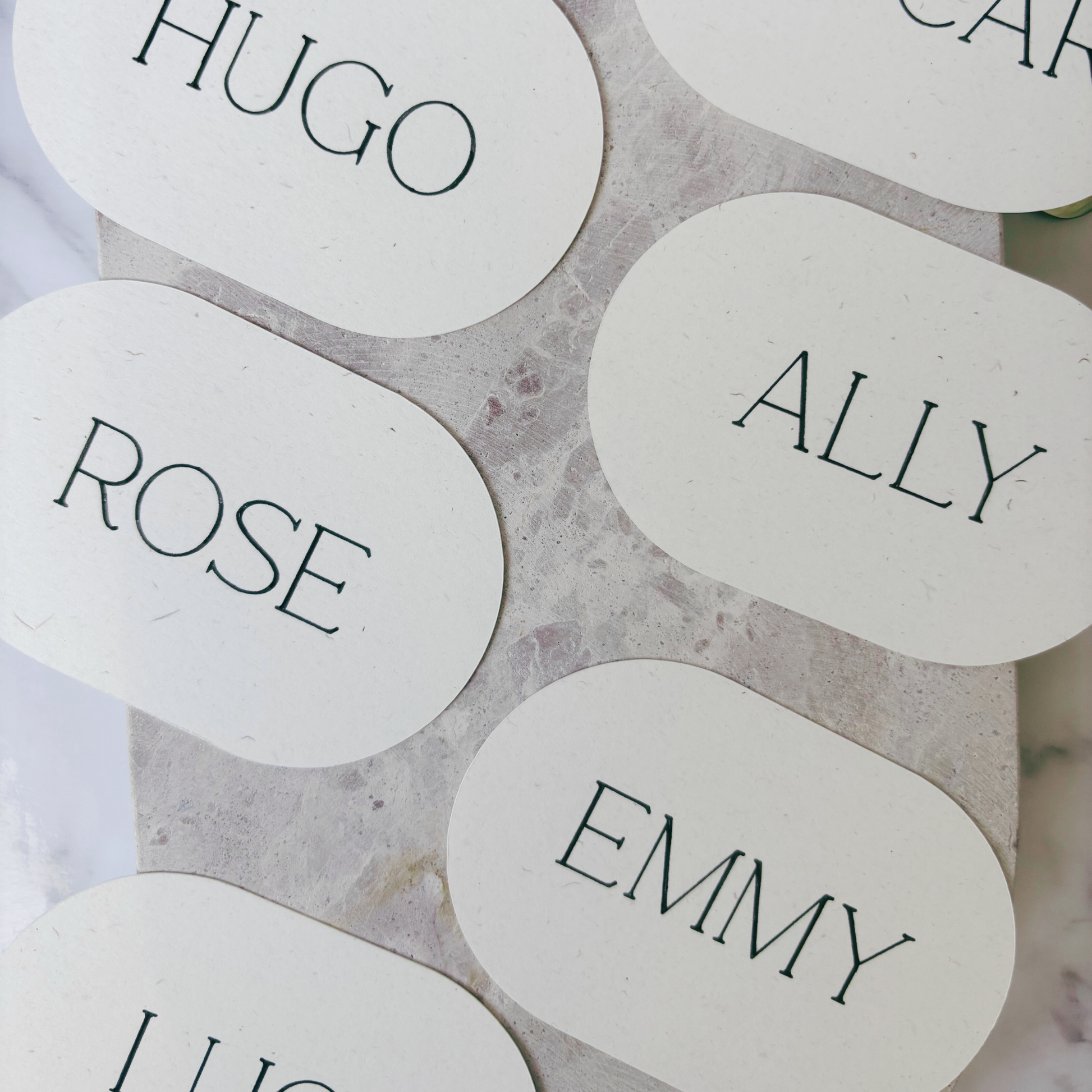 Flat lay of oval ivory place cards with printed guest names, styled for wedding table décor