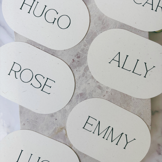 Flat lay of oval ivory place cards with printed guest names, styled for wedding table décor