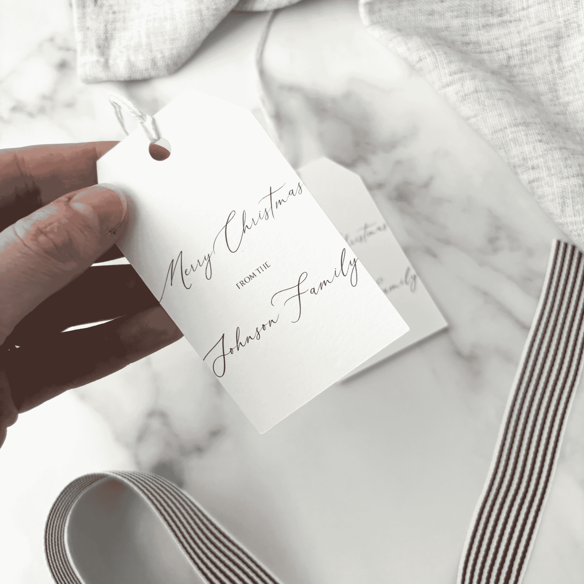 Custom Christmas gift tag with calligraphy text and ribbon, handmade stationery detail for gift packaging