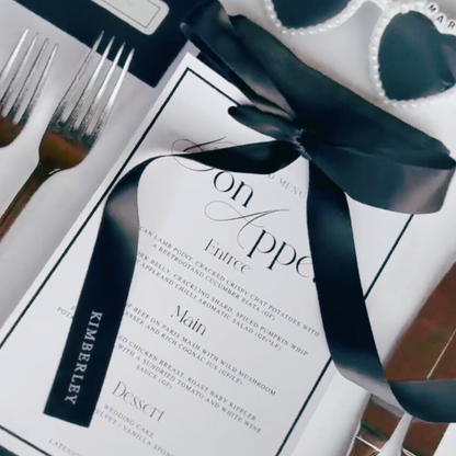 Black personalised satin ribbon tied around wedding menu, styled with modern table setting
