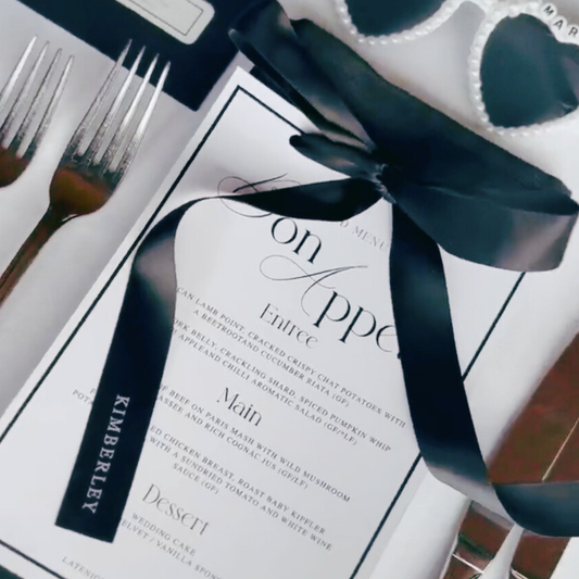 Black personalised satin ribbon tied around wedding menu, styled with modern table setting