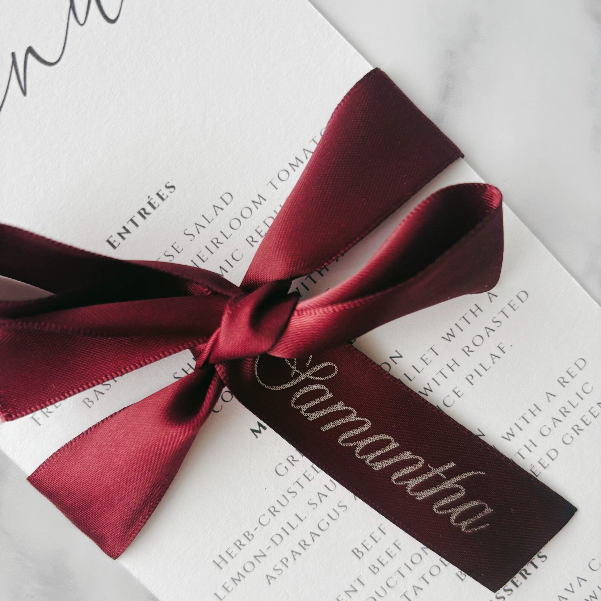 Burgundy printed ribbon tied in bow around wedding menu with custom guest name