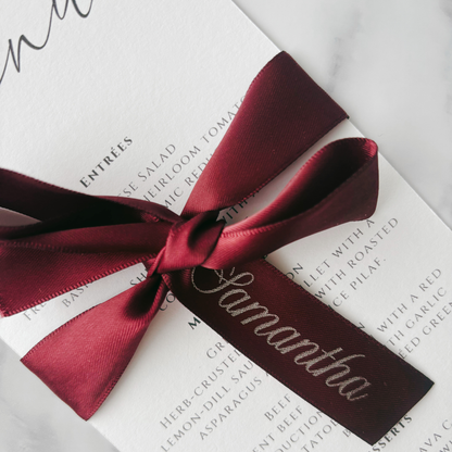 Burgundy printed ribbon tied in bow around wedding menu with custom guest name