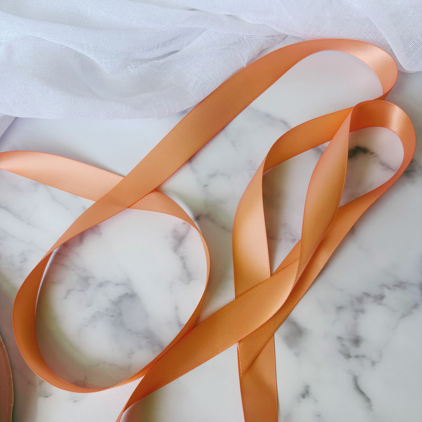 Peach satin ribbon for wedding invitations and gift wrapping, styled on marble background