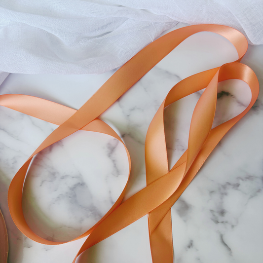 Peach satin ribbon for wedding invitations and gift wrapping, styled on marble background