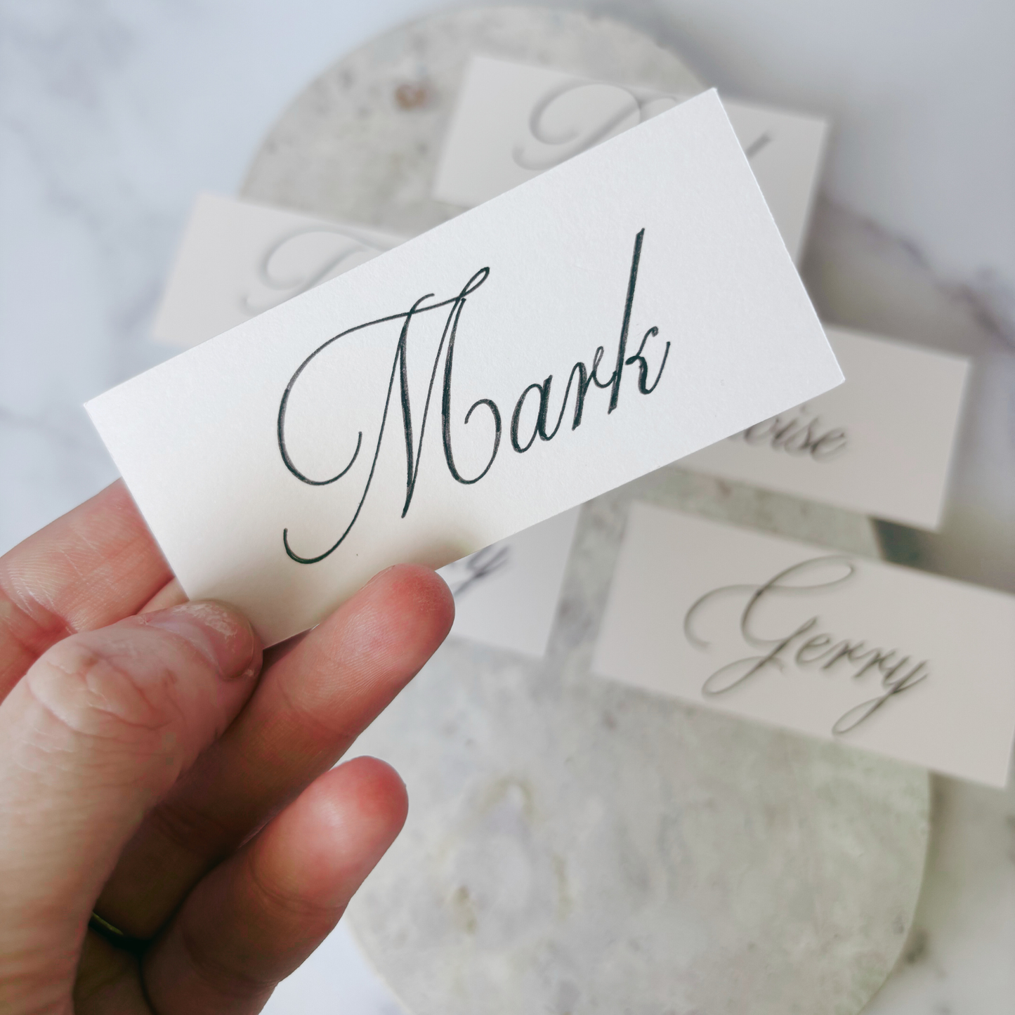 Close-up of nude rectangular wedding place card with handwritten-style guest name