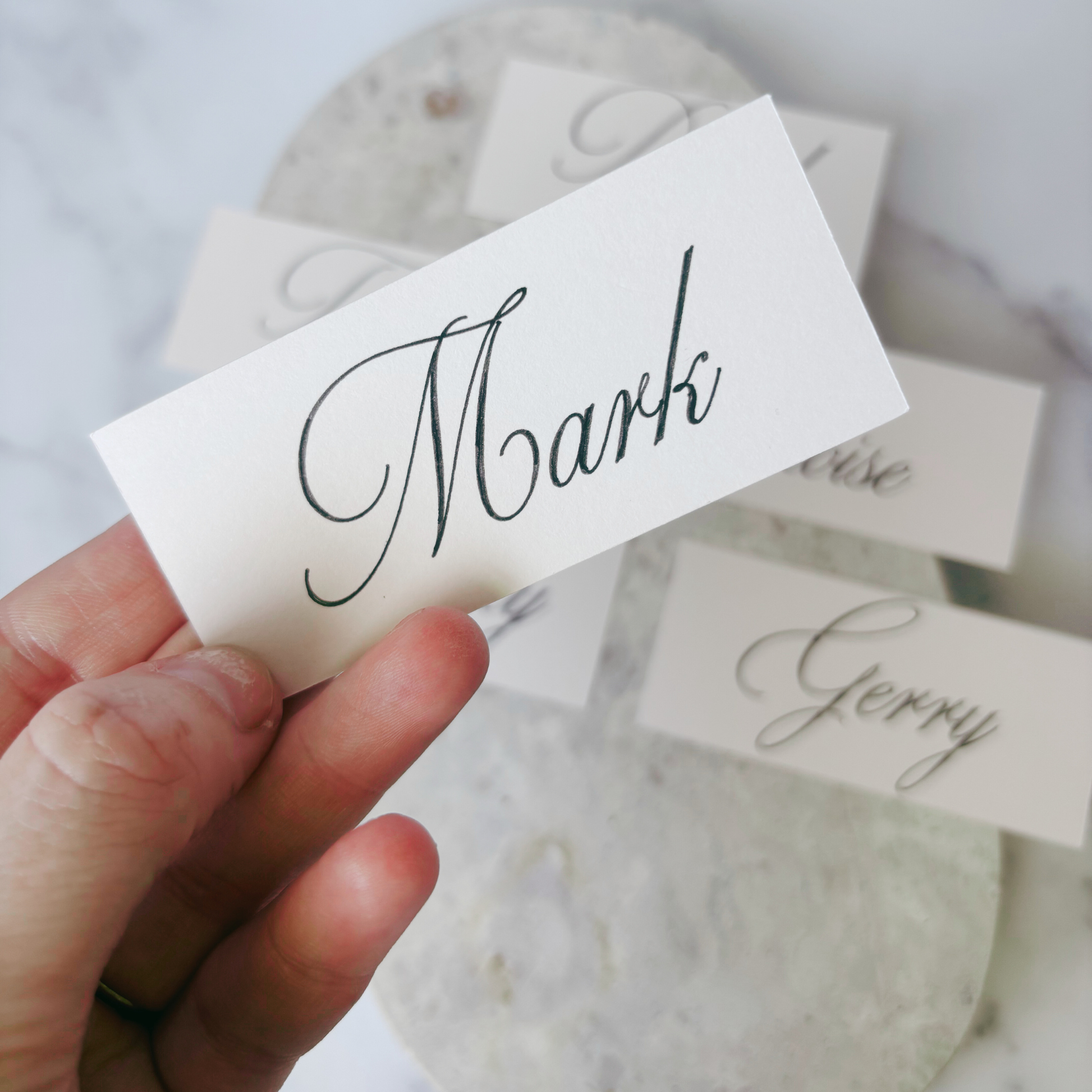 Close-up of nude rectangular wedding place card with handwritten-style guest name