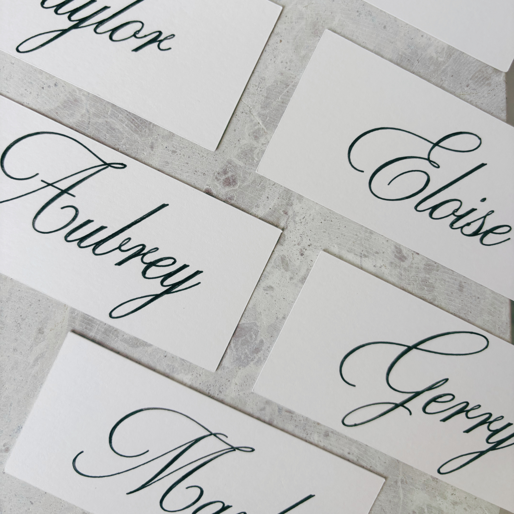 Flat lay of nude rectangular place cards with personalised names, styled on stone surface