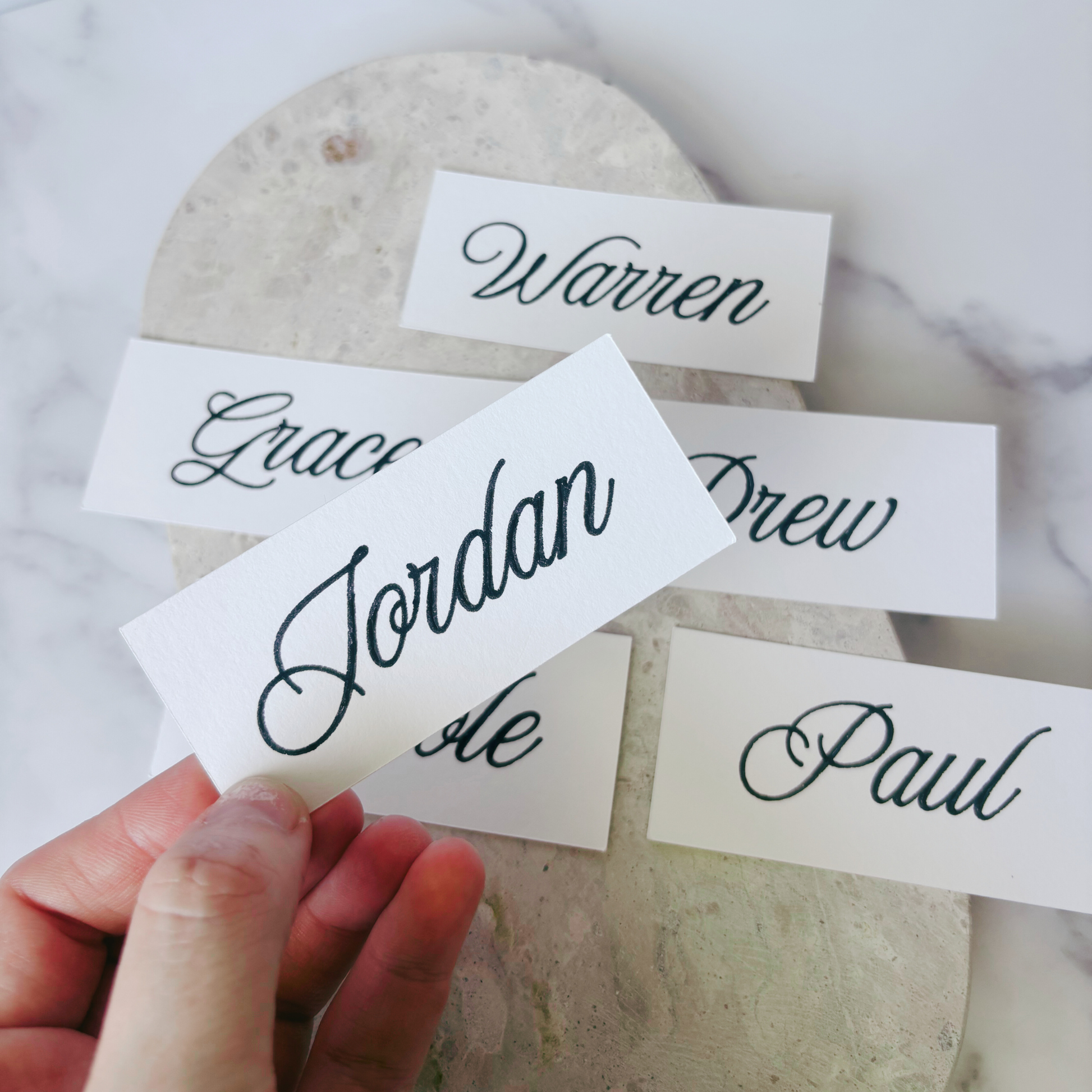 Close-up of white rectangular wedding place card with handwritten guest name