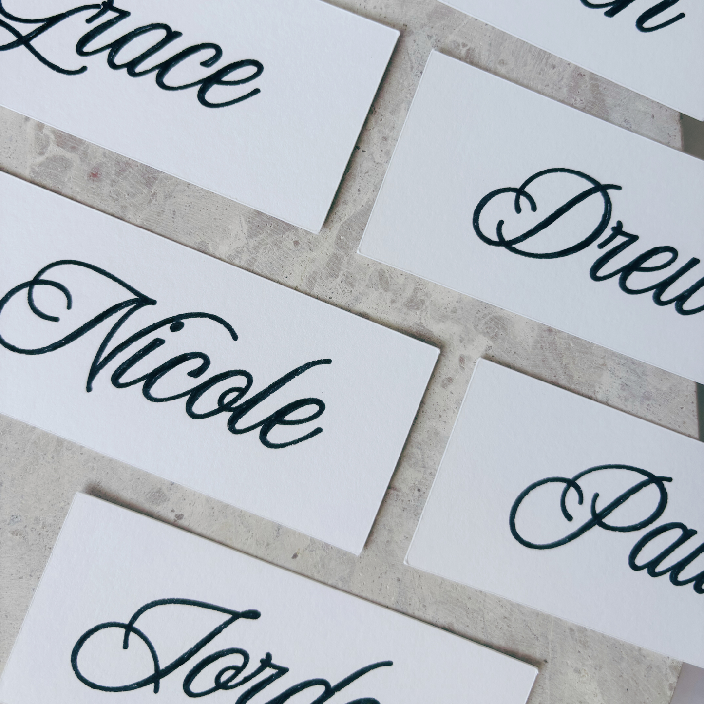 Flat lay of white rectangular place cards with handwritten names, styled for wedding tables