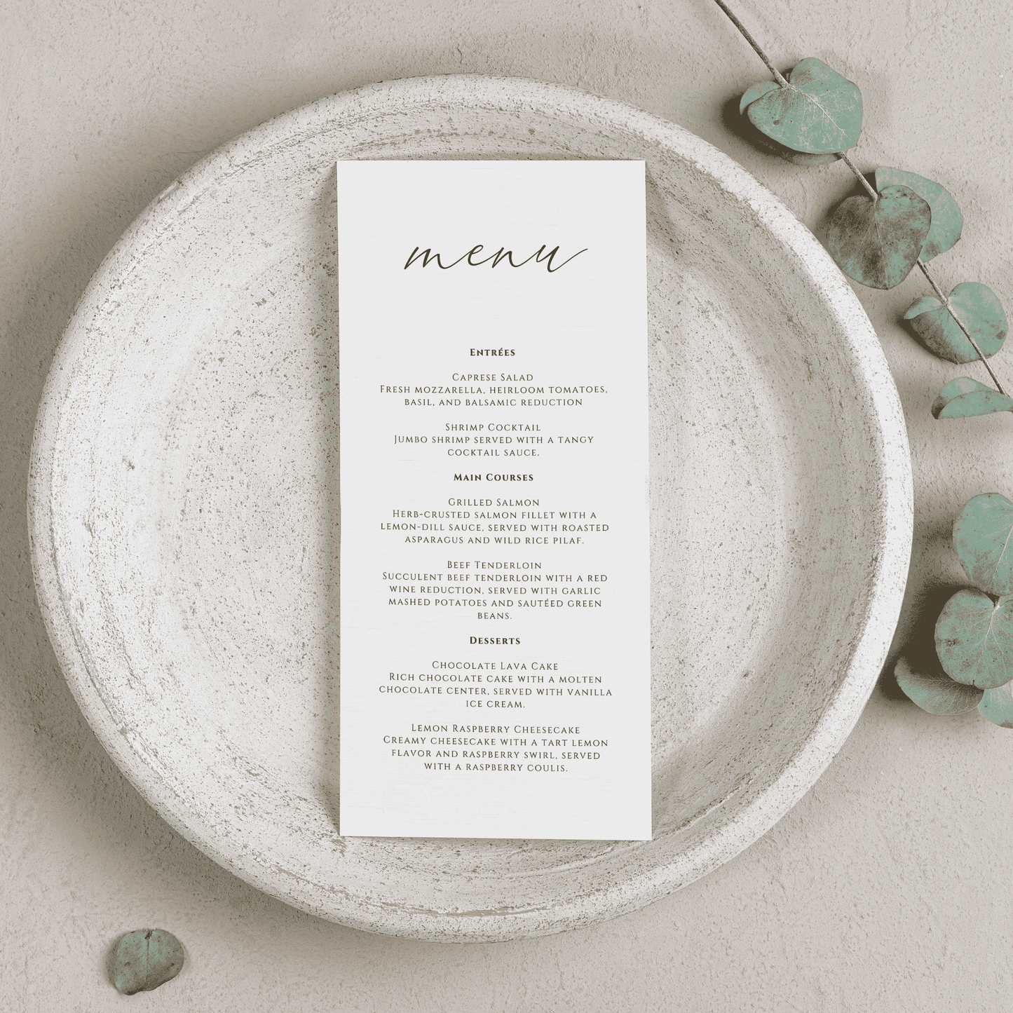 Printed wedding menu displayed on a stone plate with soft greenery, designed to complement custom wedding invitations and event table settings
