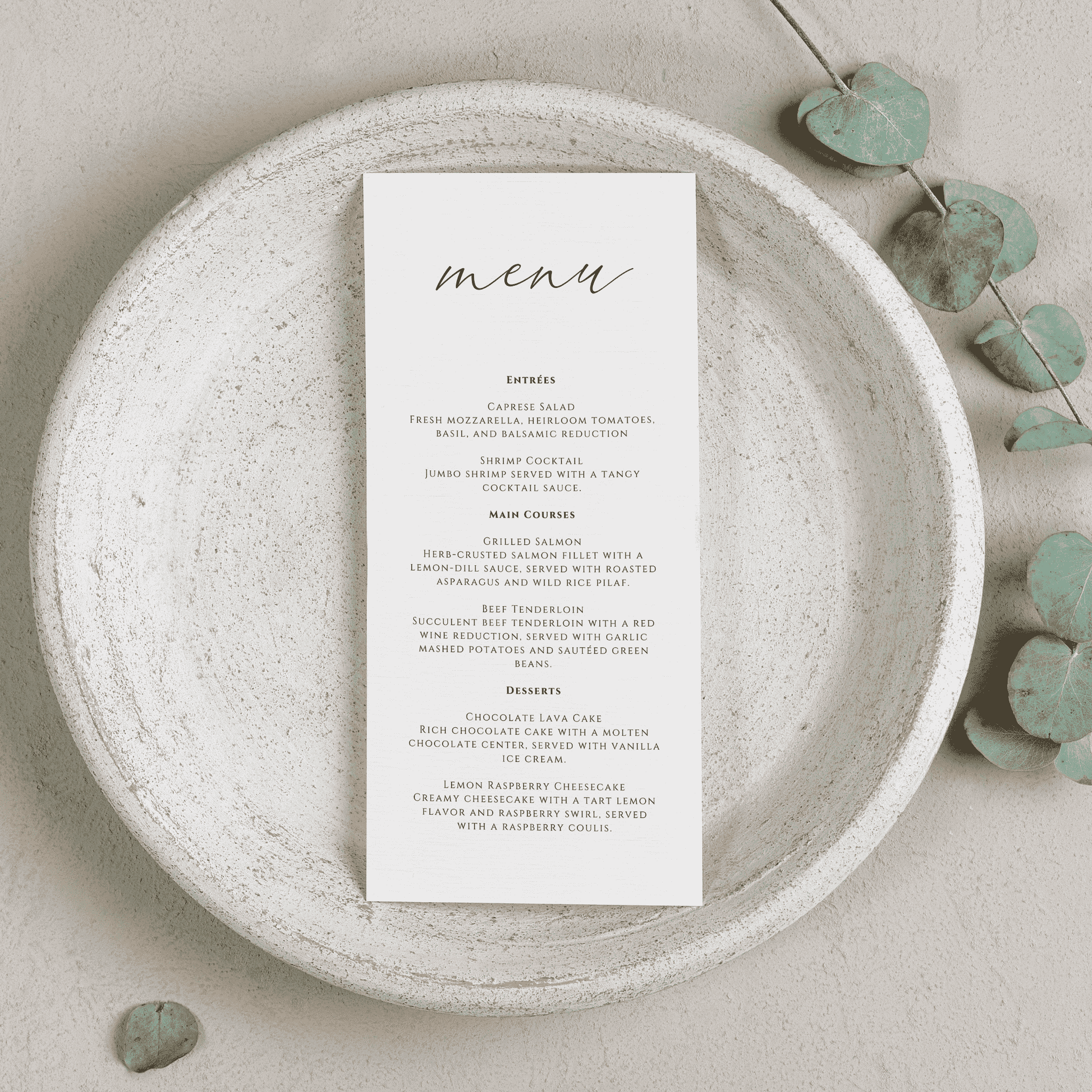 Printed wedding menu displayed on a stone plate with soft greenery, designed to complement custom wedding invitations and event table settings