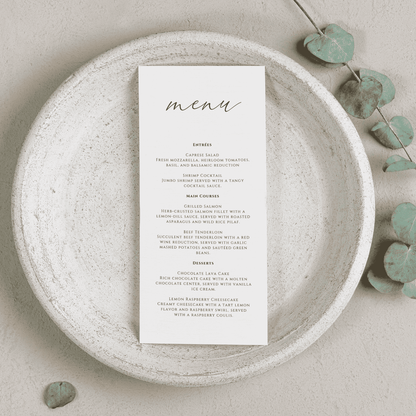 Printed wedding menu displayed on a stone plate with soft greenery, designed to complement custom wedding invitations and event table settings